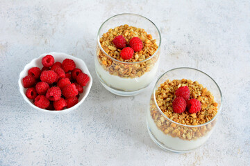 two glasses of raspberries, granola and yogurt with a bowl of raspberries top view