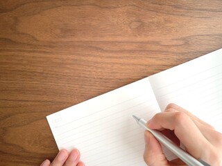 Obraz premium デスクでノートに字を書く女性の手元