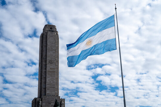 Bandera Argentina izada en altura y flameando al viento con el Monumento Nacional a la bandera de fondo
