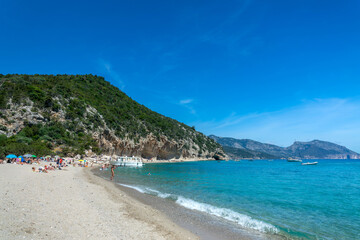 People and boats at Cala Luna beach and clear transparent blue water in the Gulf of Orosei, Sardinia island, Italy