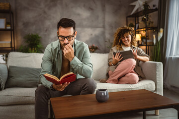 Obraz premium Boyfriend read a book while his girlfriend use tablet at home
