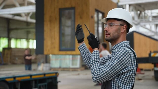 Foreman with walkie talkie manages the loading of a prefabricated modular house to truck