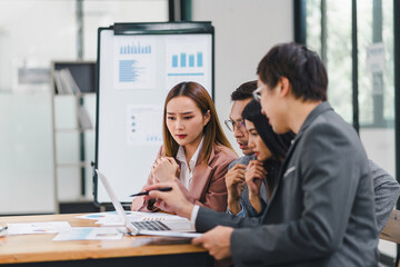 Business team serious discussion, analyzing data on laptop and documents during meeting in modern office.