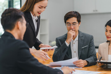 Diverse business team analyzing data and discussing strategies during an office meeting, using documents and a laptop.