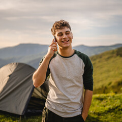 Young boy stand in front tent and talk on mobile phone on the mountain