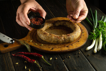 Man hands adding aromatic spices to meat sausage on cutting board. Concept of cooking delicious lunch with meat sausage at home.