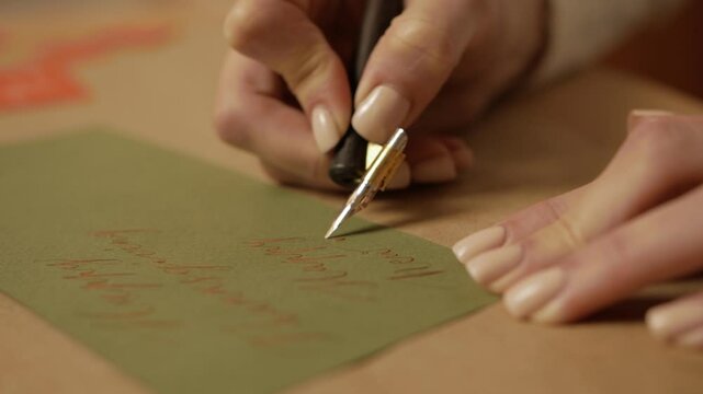 table with cardboard, stationery, nib pen, calligraphy tools. woman is writing by hand with wood nib pen.  ink lettering, calligraphy stationery. palette of paints, calligraphy ink. 