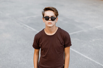 Cool fashion young man with hairstyle with sunglasses in a T-shirt on the street