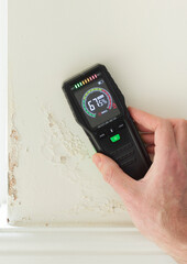 Moisture meter against a wall with rising damp, UK home interior