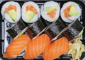 Detail closeup of plastic box Futomaki or Maki Sushi traditional thick nori seaweed leaves roll with colorful avocado salmon ingredients and fish Nigiri (focus on center)