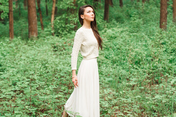 beautiful young girl in a knitted sweater with a skirt walks in the forest