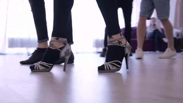 joyful dance practice in the hall on the parquet. reflection of dancing couples in the mirror. teachers show salsa and ballroom dancing movements.female legs in high heel shoes. legs of a man in shoes