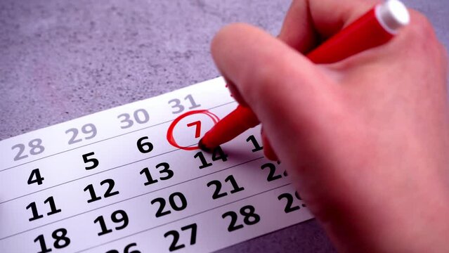 Plan a work week. Circle and strike through calendar dates. Write with a red marker. Hand planning dates. Seven