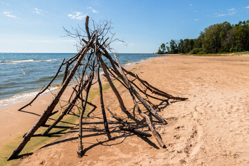 A teepee made from driftwood stands along on the silent beach sand at Harrington Beach State Park,...