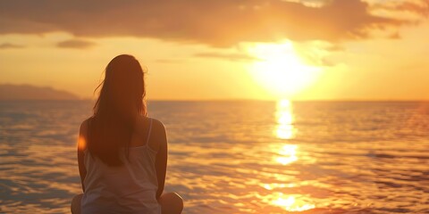 Fototapeta premium Woman sitting by ocean watching sunset from behind. Concept Portrait Photography, Outdoor Photoshoot, Sunset Ambiance, Mood Capture, Ocean View