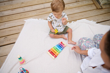 Toddler playing xylophone with parent on wooden deck