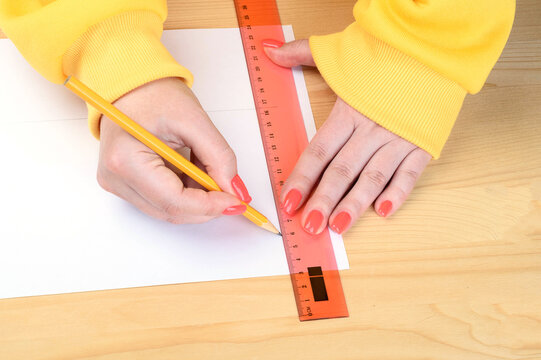 Women's hands draw lines on paper using a ruler and pencil.