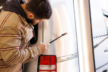 Caucasian boy uses the hammer to repair the wing of a car damaged by the accident