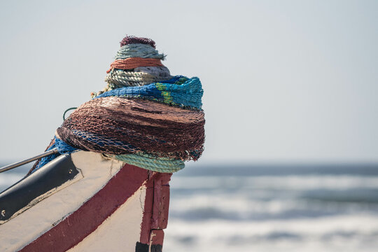 Close up shot of torn and used ropes hanging by the nose of a small wooden traditional fishing boat in the coast of Portugal, with waves breaking on the background