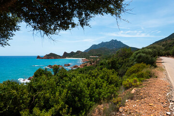 Obraz premium Picturesque road above wild Su Sirboni beach and red rock formations in province of Nuoro on Sardinia (Sardegna) island in Italy. Tyrrhenian Sea.