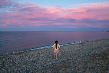 Little girl watching pink sunset on Perd'e Pera beach on Sardinia island,Italy in May, Tyrrhenian Sea. Golden hour.