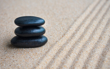 Black zen stones with lines carved on sand background