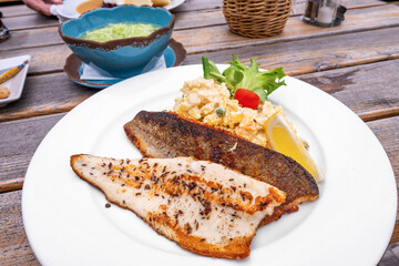Potato salad with trout fillet, part of blue bowl with cucumber salad.