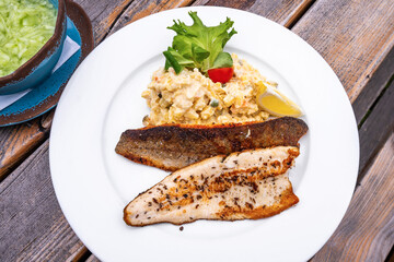 Potato salad with trout fillet and cucumber salad on wooden table.