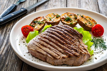 Grilled beef steak with baked potatoes and fresh vegetables on wooden table