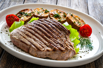 Grilled beef steak with baked potatoes and fresh vegetables on wooden table