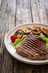 Grilled beef steak with baked potatoes and fresh vegetables on wooden table