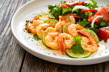 Fried shrimps with garlic, lime and fresh vegetables served on white plate on wooden table

