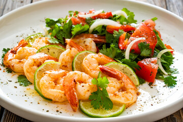 Fried shrimps with garlic, lime and fresh vegetables served on white plate on wooden table
