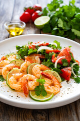 Fried shrimps with garlic, lime and fresh vegetables served on white plate on wooden table
