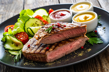 Grilled beef steak with sauces and fresh vegetables on wooden table