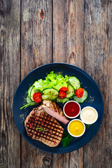 Grilled beef steak with sauces and fresh vegetables on wooden table