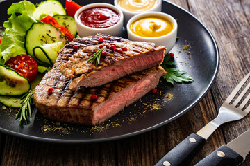 Grilled beef steak with sauces and fresh vegetables on wooden table