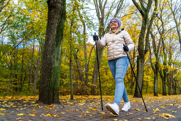 Nordic walking - one mid-adult beautiful woman exercising in city park using Nordic walking poles