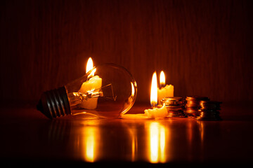 Incandescent lamp and candle and stacks of coins in the dark at home, without light, no money to...