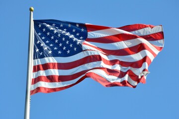 Obraz premium A vibrant image of the United States flag waving against a clear blue sky. The American flag is prominently displayed with its red, white, and blue colors and stars and stripes pattern.