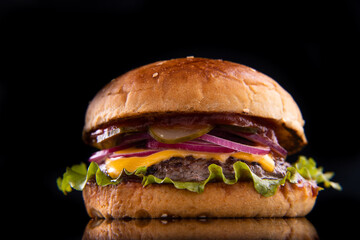 Burger with beef, cheese, vegetables on black plate. Dark Background. Close up.