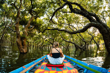A young woman sitting in a traditional wooden boat exploring the natural scenery of  mangrove...