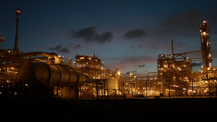 Fototapeta premium Aerial view of chemical plants at night, in an Industrial Park, with pipelines and chimneys throughout the factories and lights glowing in the petrochemical industry estate