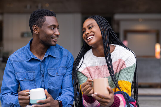 Holding mugs and smiling, young Black couple enjoying time together at home
