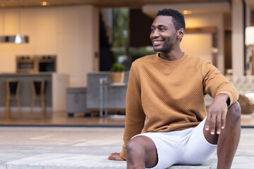 Sitting on steps, man in casual clothes and white shorts smiling and looking away, copy space