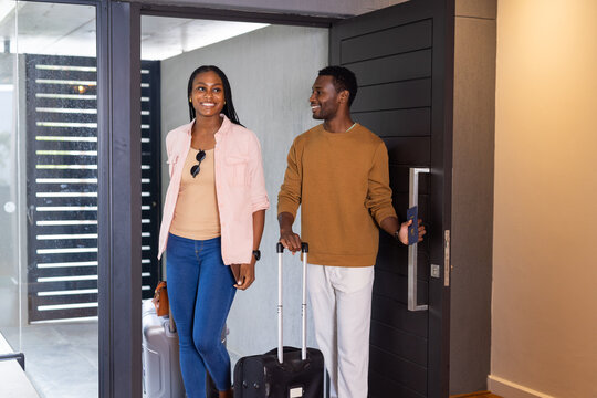Arriving vacation home, young African American couple entering with luggage, smiling - Powered by Adobe