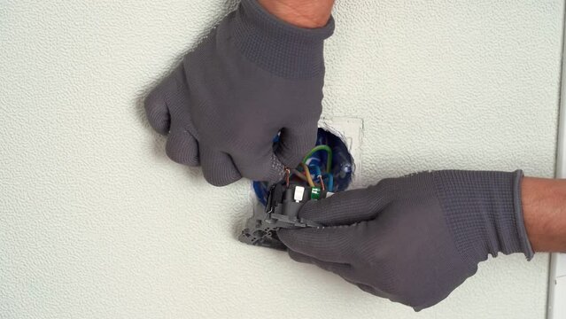 Hands of electrician insert wires of junction box in electrical outlet into terminals clips. Replacing electrical outlet. Installing electrical socket. Electricity