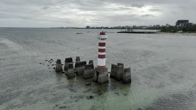 Drone flies over Farol da Ponta Verde toward Marco dos Corais on overcast day in Maceio, Alagoas, Brazil