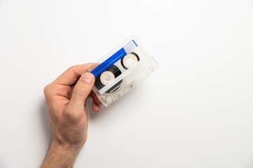 An unrecognizable male hand holds a retro audio cassette on a white background. Using magnetic audio cassettes