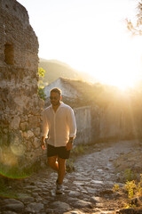 A young man walks in a lush, green outdoor setting at sunset, bathed in warm, golden light. He gazes upwards in contemplation, creating a serene and peaceful atmosphere.